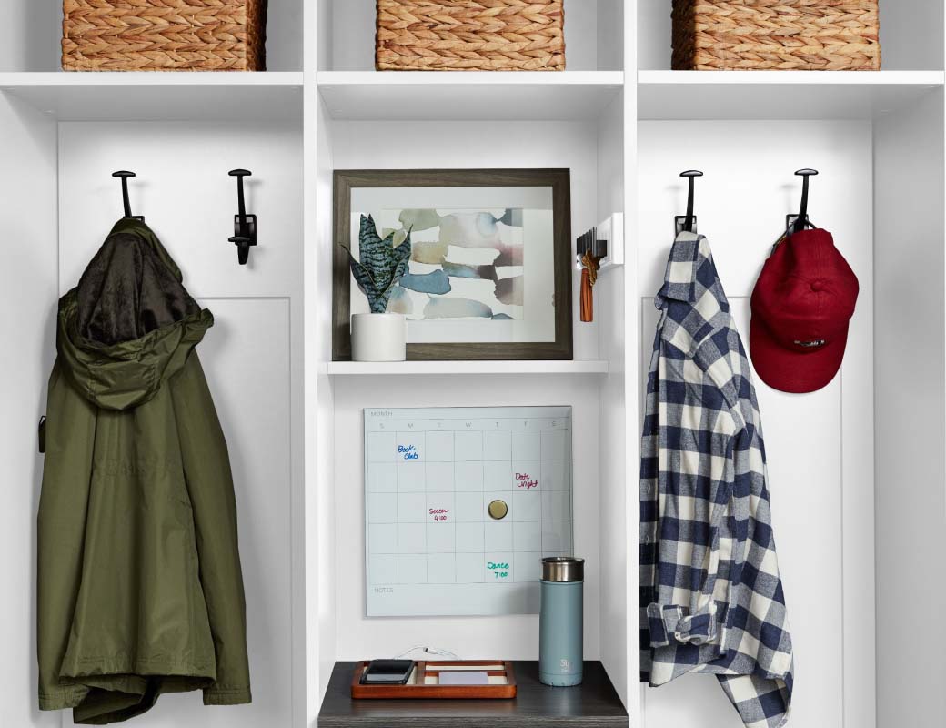 An organized closet with a green coat, flannel shirt, and red hat hung up.