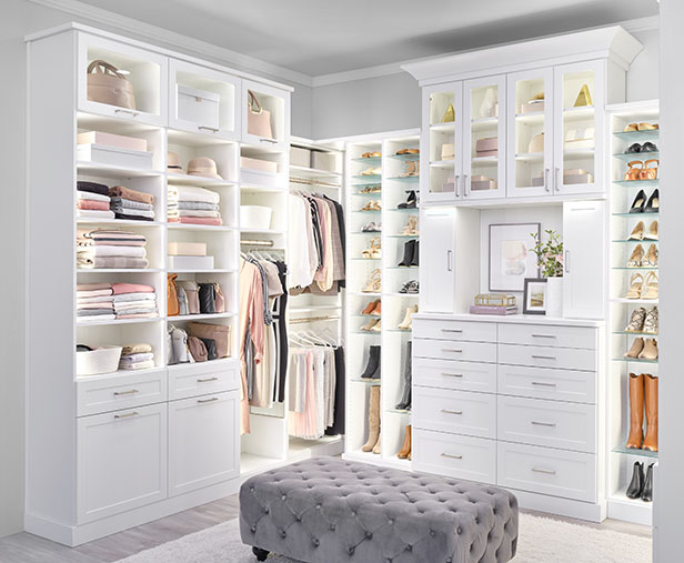 An organized white closet with a bench in the center.