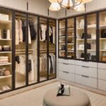 Large boutique closet for her with glass-front cabinets with light tone panels and onyx frames and pulls, soft-close drawers with light colored fronts and onyx hardware, closed cabinets above, and integrated lighting