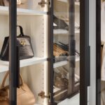 Close up of custom glass-front cabinets with light tone panels and onyx frames, holding a variety of purses and shoes