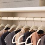 Close up of a boutique closet with a Winter white leather hanging rod and black end caps, and an open shelf with storage box above