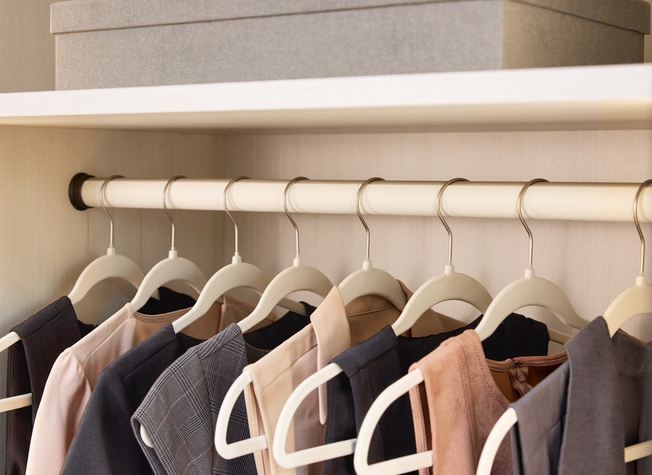 Close up of a boutique closet with a Winter white leather hanging rod and black end caps, and an open shelf with storage box above