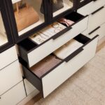 Close up of custom storage in a boutique closet, soft-close drawers with light colored fronts holding jewelry and sweaters, glass-front cabinets with onyx frames holding purses