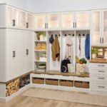 Entryway 1 Custom entryway with glass-front cabinets above, and a mix of solid doors, hook storage, open shelves, wicker baskets, and soft-close drawers below holding coats, firewood, backpack, and personal items, in a warm white finish, medium wood tone tops, and matte black hardware