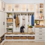 Entryway 2 Custom entryway with glass-front cabinets above, and a mix of solid doors, hook storage, open shelves, wicker baskets, and soft-close drawers below holding coats, firewood, backpack, and personal items, in a warm white finish, medium wood tone tops, and matte black hardware