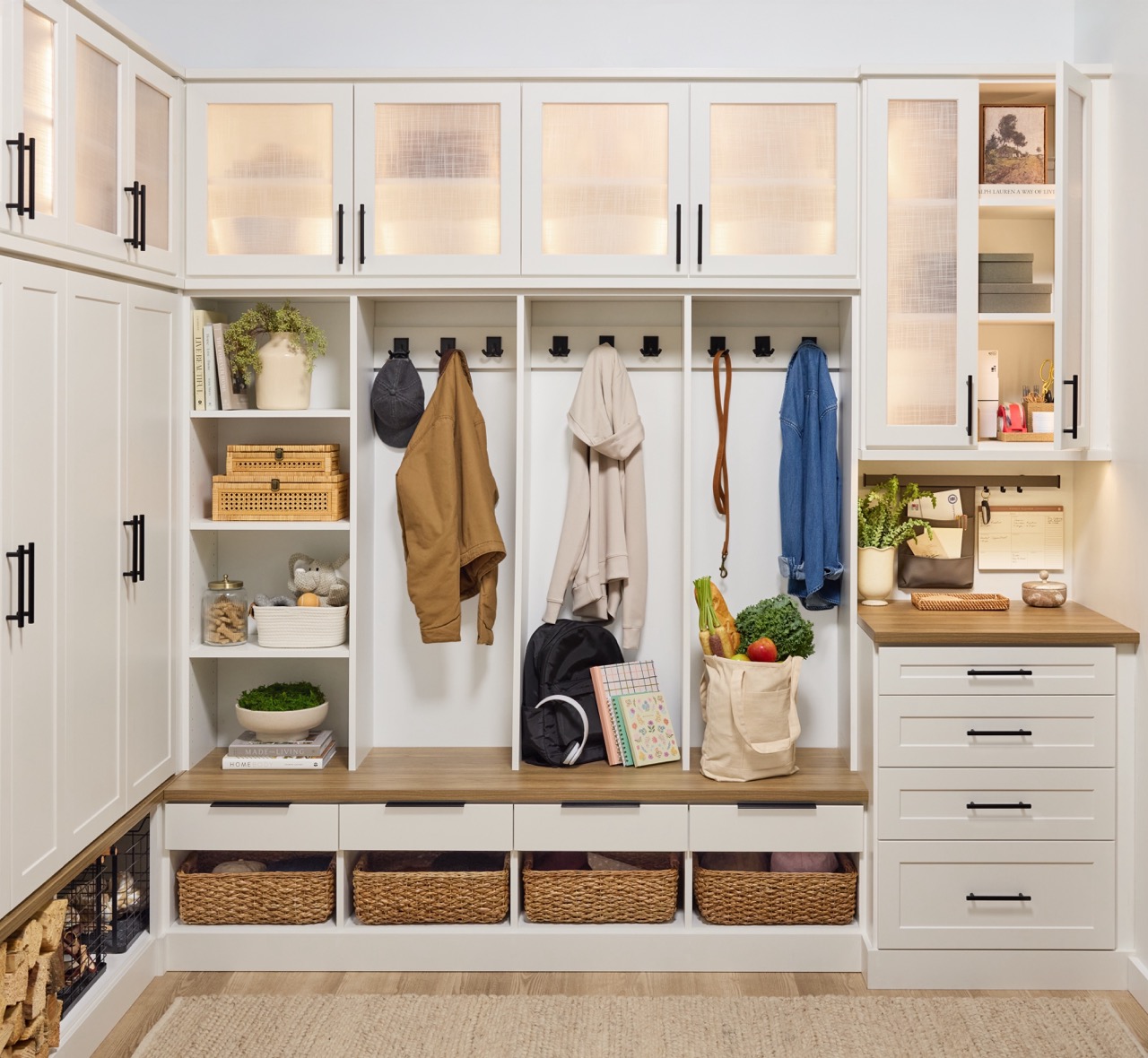Entryway 2 Custom entryway with glass-front cabinets above, and a mix of solid doors, hook storage, open shelves, wicker baskets, and soft-close drawers below holding coats, firewood, backpack, and personal items, in a warm white finish, medium wood tone tops, and matte black hardware