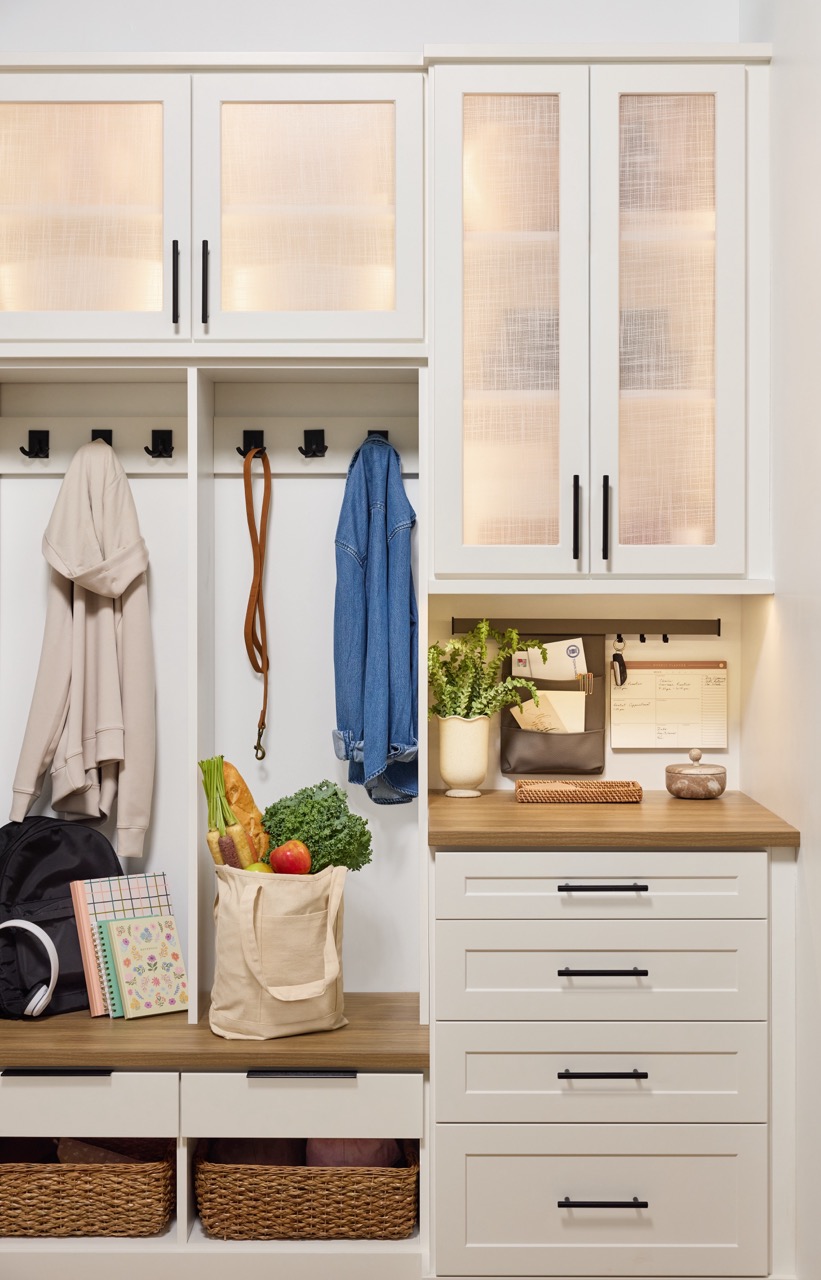 Entryway 3 Custom entryway with glass-front cabinets above and a mix of hook storage, open shelves, and soft-close drawers below to hold coats, easy drop zone items, and accessories, in a warm white finish, medium wood tone tops, and matte black hardware