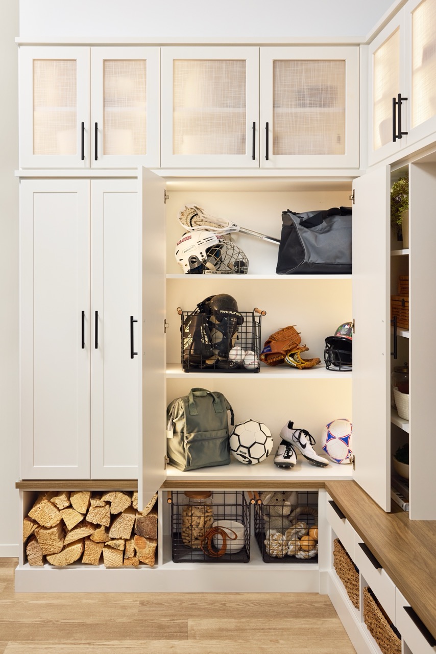 Entryway 4 Custom entryway with glass-front cabinets above and locker-style cabinets below for sports equipment, firewood, and miscellaneous storage in a warm white finish with matte black hardware