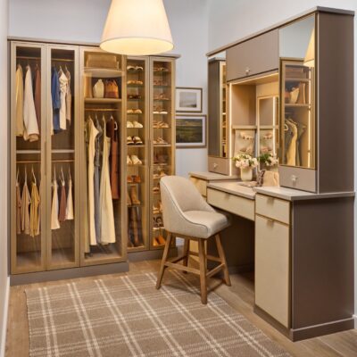 Her custom closet in daylight with glass-front cabinets for clothes and shoe organization, and a vanity with soft-close drawers, integrated lighting, mirrored door fronts, leather drawer fronts, and matte brass and gold accents