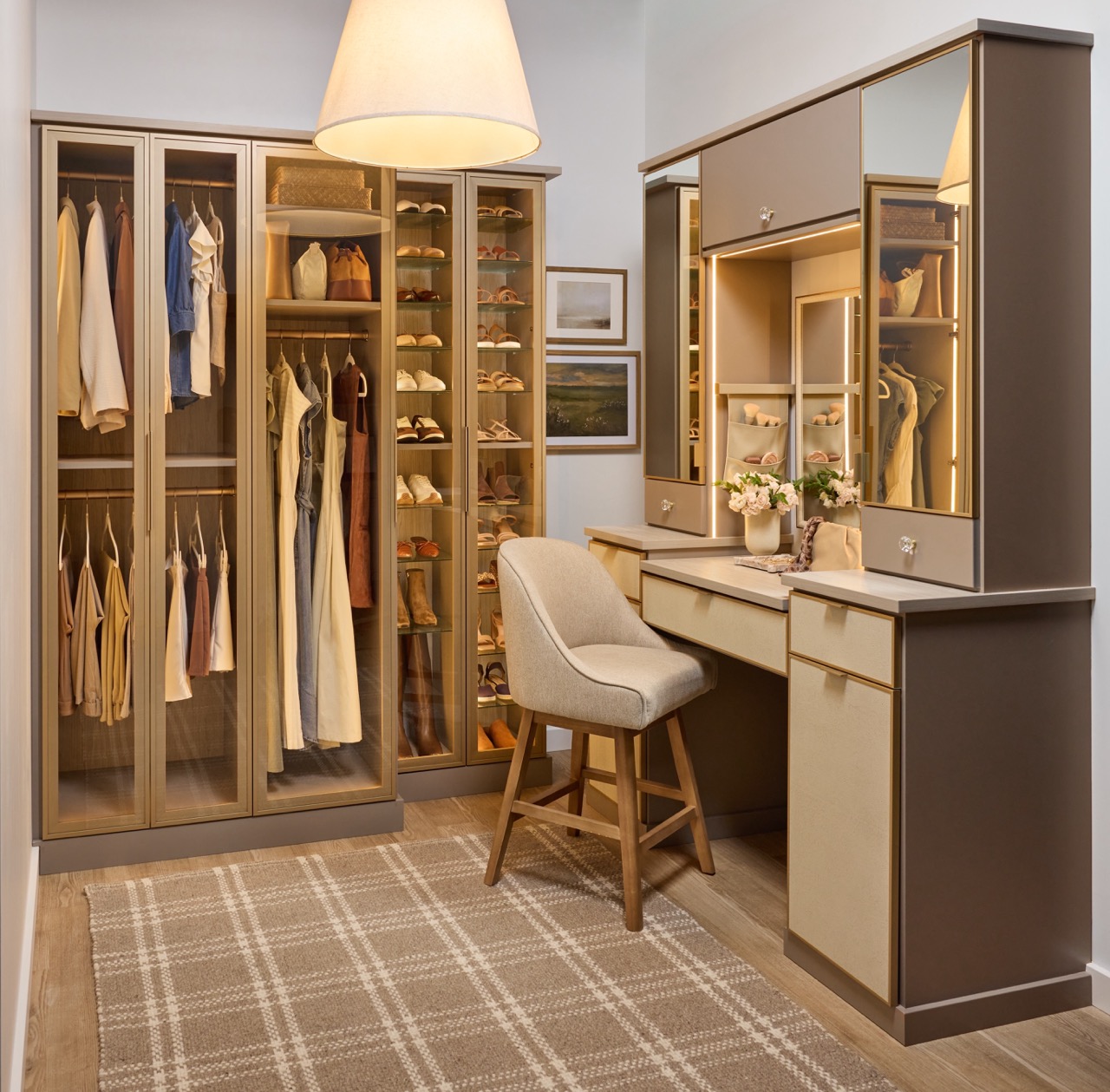 Her custom closet in daylight with glass-front cabinets for clothes and shoe organization, and a vanity with soft-close drawers, integrated lighting, mirrored door fronts, leather drawer fronts, and matte brass and gold accents