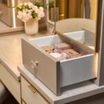 Close up of a custom vanity with soft-close drawers, mirrored door fronts, integrated lighting, leather drawer fronts, and matte brass and gold accents