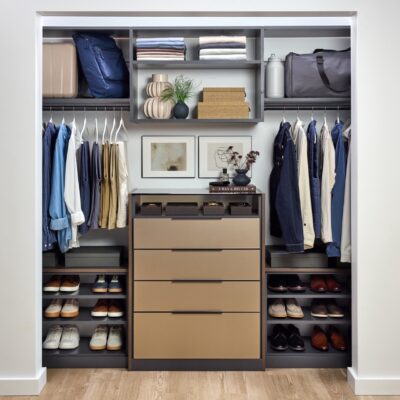 His reach-in closet featuring soft-close drawers with Seared brown fronts, hanging clothes rods, open shelf storage holding shoes, duffle bag, folded clothes, personal items and accessories, in a mix of medium wood and onyx tones, Elusion glass top, and matte black hardware