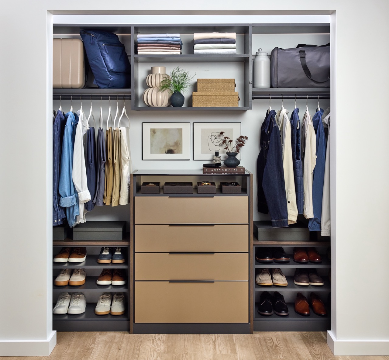 His reach-in closet featuring soft-close drawers with Seared brown fronts, hanging clothes rods, open shelf storage holding shoes, duffle bag, folded clothes, personal items and accessories, in a mix of medium wood and onyx tones, Elusion glass top, and matte black hardware