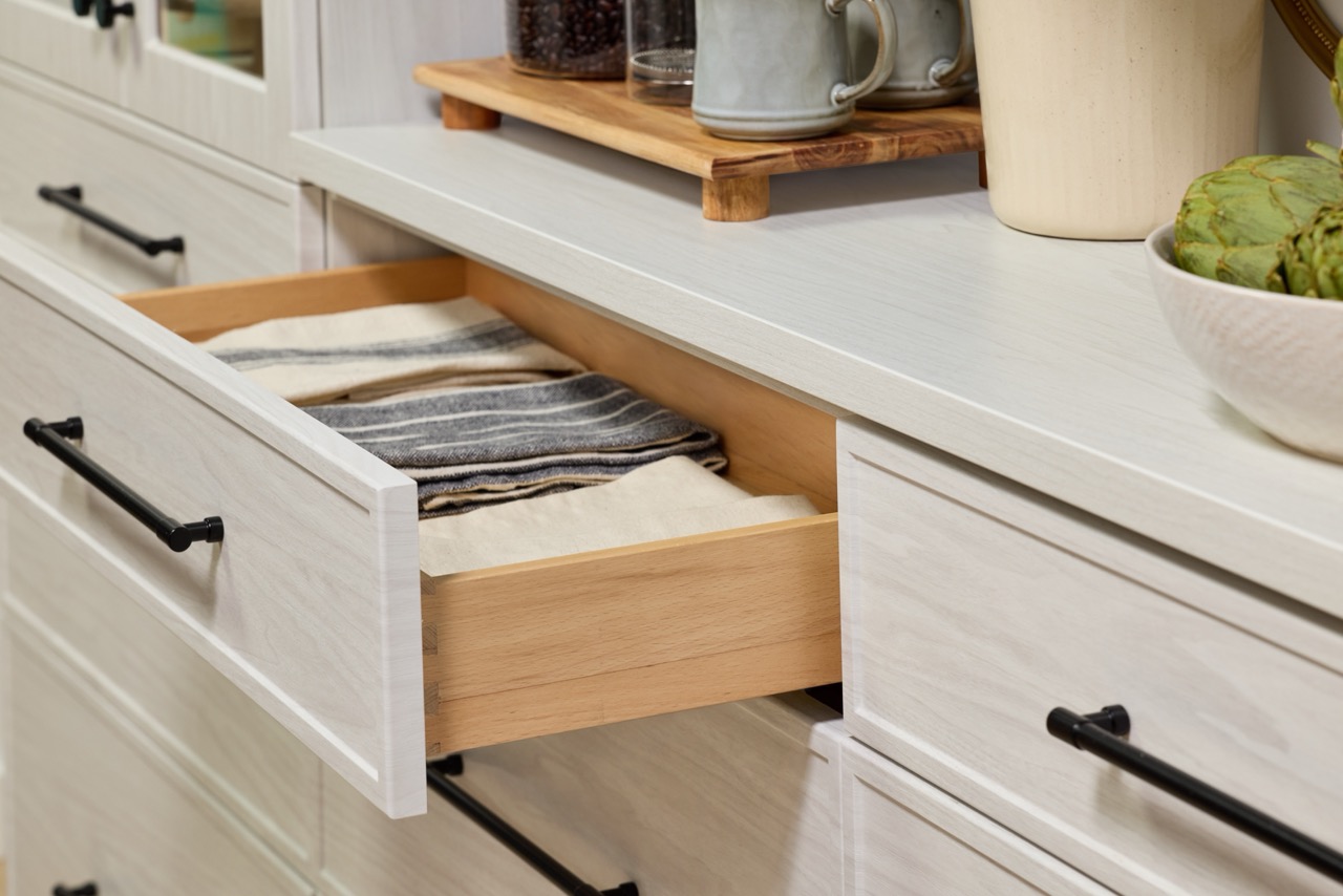 Detail of a custom hutch soft-close drawer in a light wood-tone finish with black hardware, opened to show linens inside