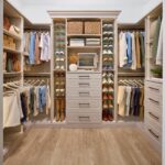 Shared walk-in closet for a man and woman in a light wood-tone finish with custom storage, Shoe Shrine, valet rod, and belt rack