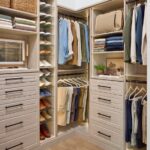 Shared walk-in closet in a light wood-tone finish with custom storage, Shoe Shrine, hanging rods holding a man's shirts and pants, and storage shelves and drawers
