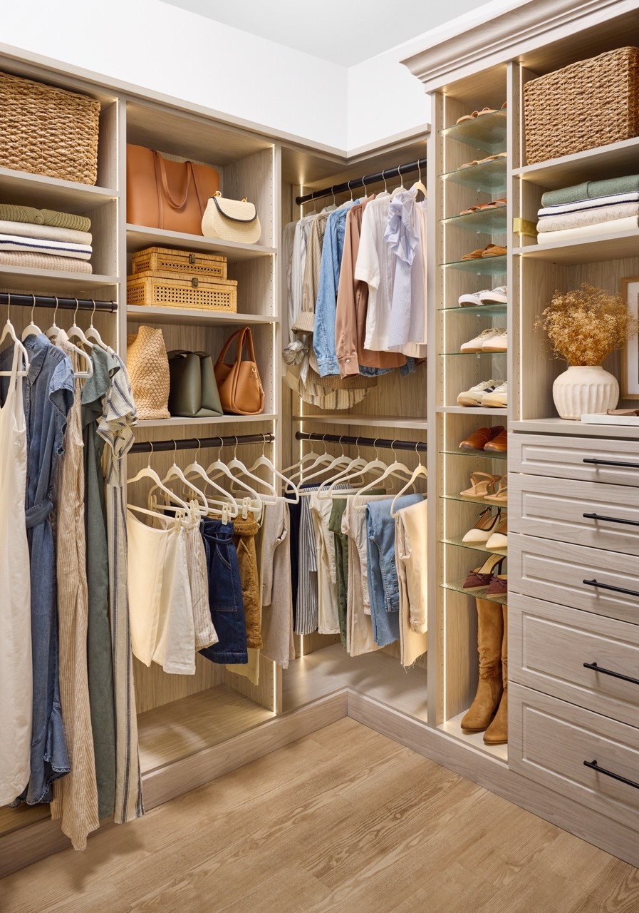 Shared walk-in closet in a light wood-tone finish with customized shelves and drawer storage, hanging rods with dresses, shirts, and pants, and a Shoe Shrine with a woman's shoes and boots