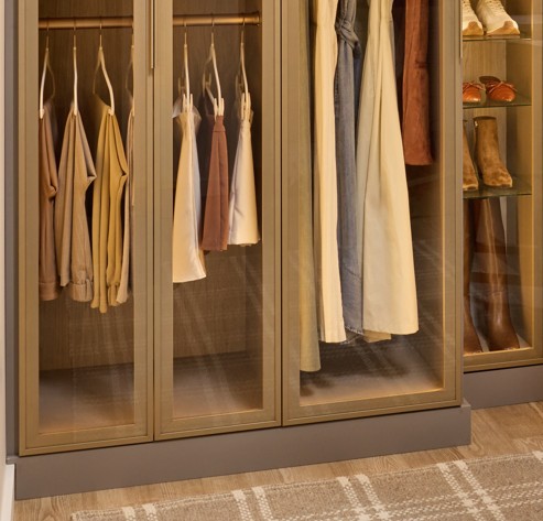 Closet storage with a variety of hanging clothes and shoes behind glass cabinet doors